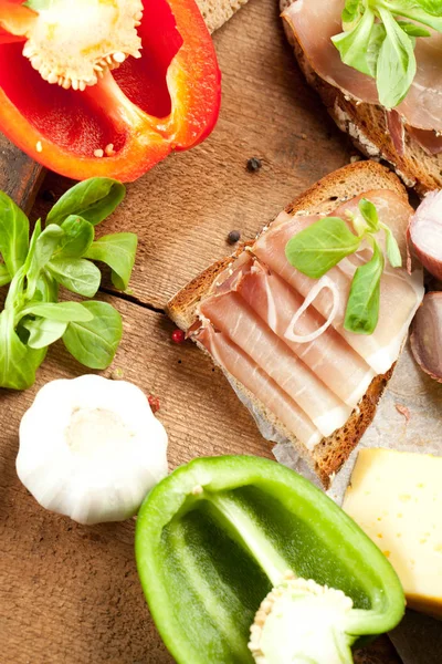 Ekmek, dilimlenmiş jambon, peynir, baharat ve sebzeli ahşap masada nefis yemek manzarası.