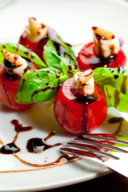 Lezzetli kiraz domates ile mozzarella ve fesleğen yaprakları beyaz tabak içinde