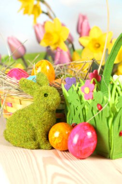 Dekoratif sepetler, parlak boyalı yumurta, çiçekler ve ahşap yüzey yeşil Paskalya tavşanı 