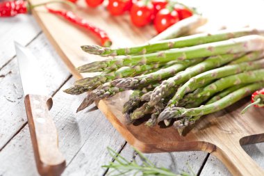 taze kuşkonmaz Ahşap doğrama tahtası, bıçak, biberiye, biber ve domates masada görmek   