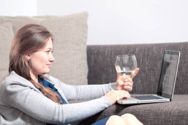 gülümseyen genç kadın şarap cam tutan ve evde dizüstü bilgisayar kullanarak yan görünümü 