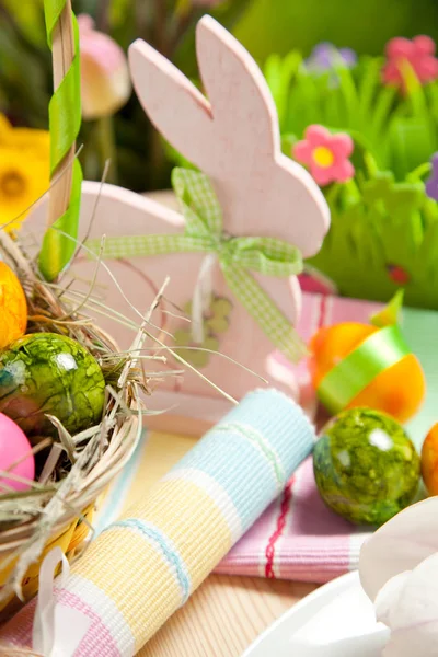 wicker basket with colorful painted eggs and wooden easter rabbit on table, selective focus