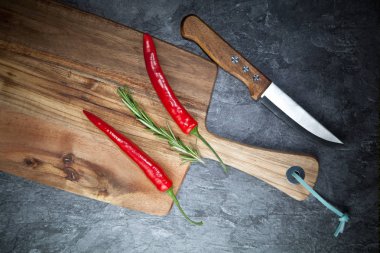 Kırmızı sıcak biber biber, biberiye, bıçak ve gri masada ahşap tahta