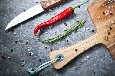 Kırmızı sıcak biber biber, baharatlar, bıçak ve gri masada ahşap tahta