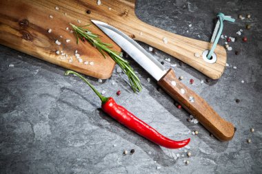 Kırmızı sıcak biber biber, baharatlar, bıçak ve gri masada ahşap tahta