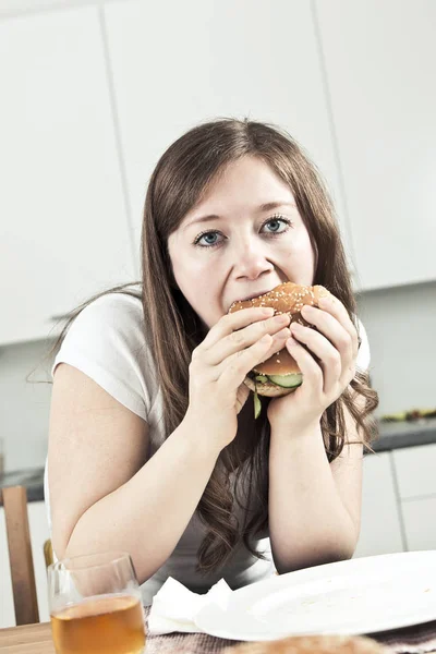 young woman eating hamburger and looking at camera
