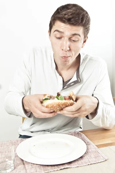 英俊的年轻人吃美味的三明治与肉和蔬菜 — 图库照片