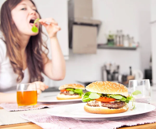 おいしいハンバーガーと後ろに野菜を食べる女性のクローズアップビュー 選択的な焦点 — ストック写真