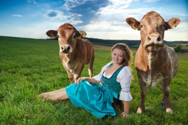 kahverengi inekler arasında oturan ve kamera gülümseyen çekici genç kadın 