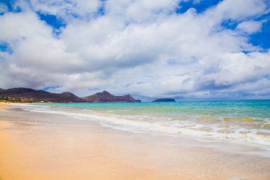 İnanılmaz kumlu sahil, deniz dalgaları ve ufuktaki dağlar. 