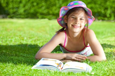 kitap ile çim üzerinde yatan ve kameraya gülümseyen sevimli çocuk