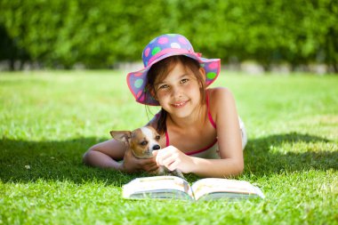 Köpek yeşil çim ve okuma kitabı üzerinde güneşli yaz gününde yalan ile şirin kız