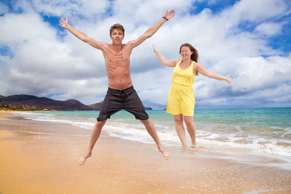 happy young couple jumping and smiling at camera on sandy beach