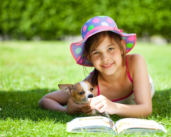 可爱的女孩与狗躺在绿草和阅读书籍在阳光明媚的夏日 — 图库照片#