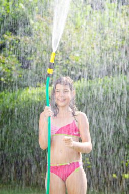 Bir bahçe hortumu ile sıcak ve güneşli yaz oynarken çok güzel genç kız