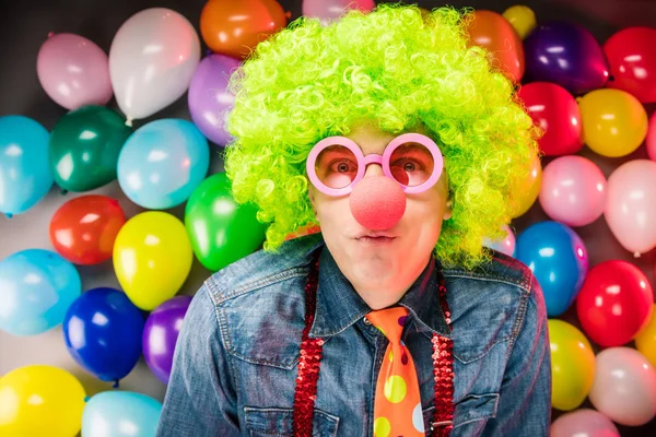 Young man in green wig and glasses posing against colorful party balloon background