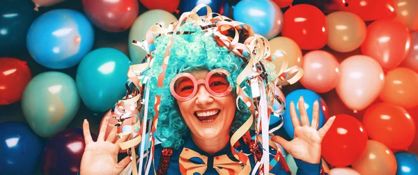 funny young woman in blue wig posing against colorful party balloon background with dozens of balloons