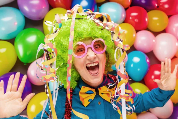 funny young woman in green wig posing against colorful party balloon background with dozens of balloons