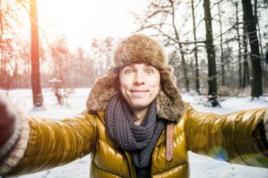 Kış ormanında kameraya gülümseyen yakışıklı genç adam.