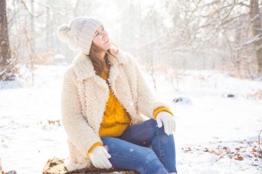 güzel oturan genç kadın gülümseyerek ve uzak kış ormanda arıyorsunuz