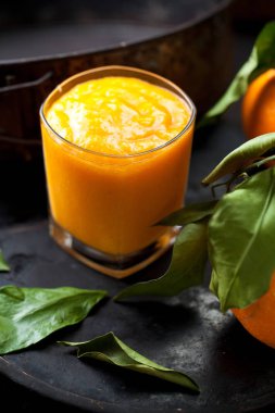 Taze turuncu smoothie ve portakal koyu arka plan üzerinde yeşil yaprakları ile
