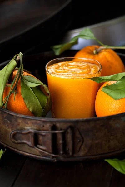 Fresh orange smoothie and oranges with green leaves on dark background