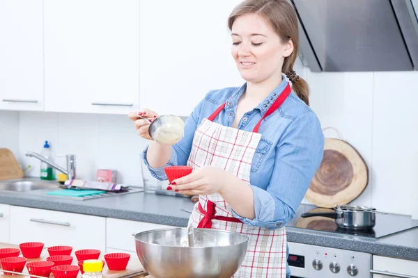 smiling young woman in apron preparing delicious cupcakes in kitchen