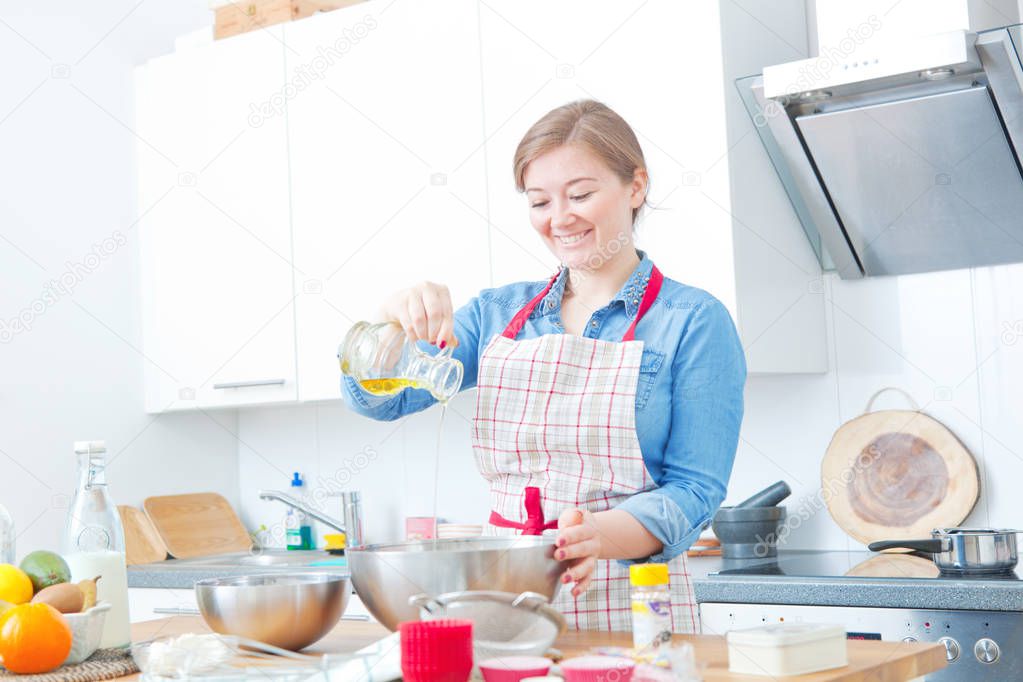 beautiful smiling young woman in apron preparing dough in kitchen