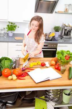 güzel genç kadın kitabı okuma ve yemek mutfakta sebze salata önlük