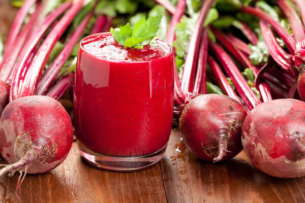 Glass of fresh beetroot juice with beets on wooden table