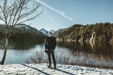 Kış dağlarında gölün yanında duran yakışıklı genç adam. 