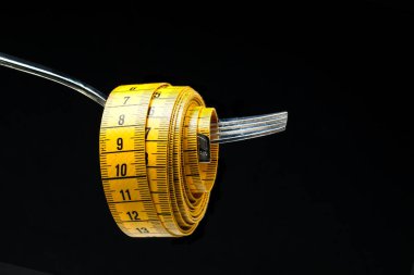 Siyah zemin üzerindeki çatal üzerindeki sarı şeritlerin yakın plan görüntüsü, diyet kavramı