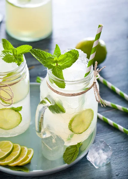 mason jars with fresh homemade lemonade, drinking straws, mint, ice cubes and lime slices