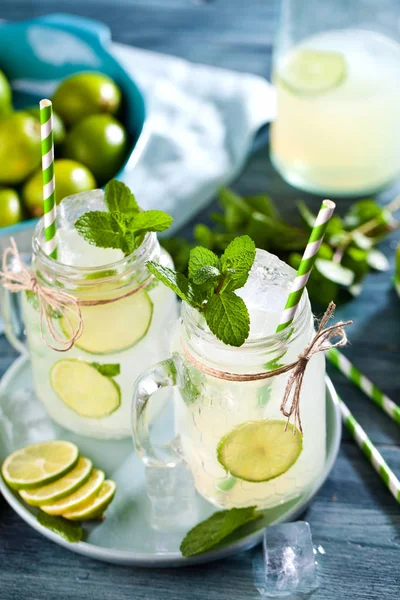 mason jars with lemonade, drinking straws, mint, ice cubes and limes