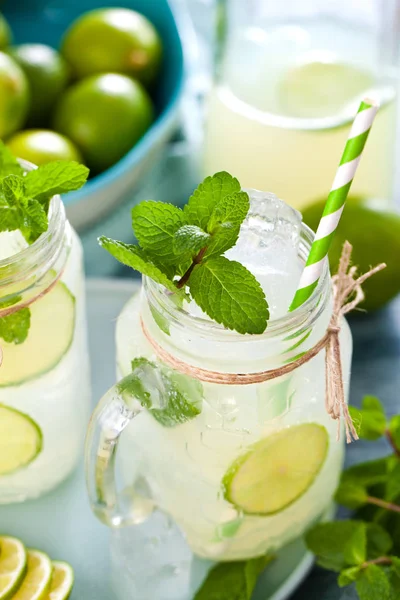 close-up view of mason jars with lemonade, drinking straws, mint, ice cubes and limes