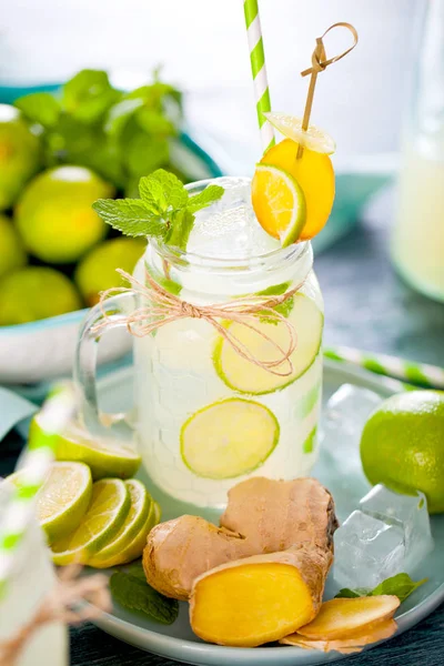 mason jar with fresh homemade lemonade, ice cubes, drinking straws and limes on wooden table