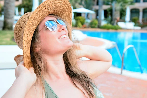 サングラスと帽子のスイミング プールのそばの夏休みを楽しんでいる美しい笑顔の若い女性 ロイヤリティフリーのストック写真