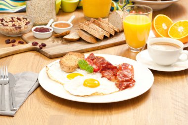 ahşap masa üzerinde sahanda yumurta ve domuz pastırması, ekmek, portakal suyu ve kahve ile lezzetli kahvaltı servisi