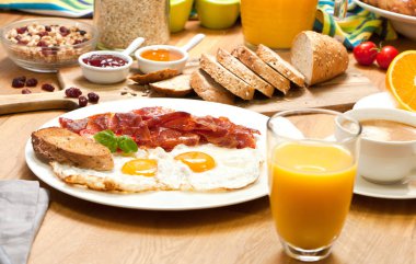 ahşap masa üzerinde sahanda yumurta ve domuz pastırması, ekmek, portakal suyu ve kahve ile lezzetli kahvaltı servisi