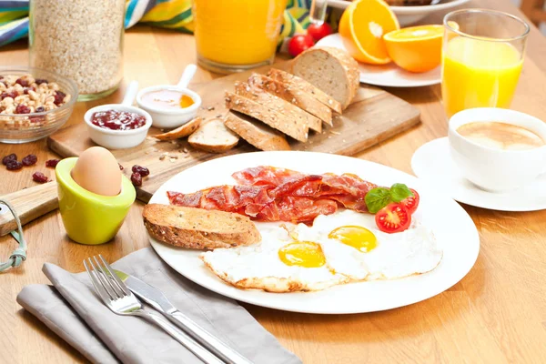 目玉焼きとベーコン チェリー トマト オレンジ ジュース コーヒー ゆで卵 ミューズリーのおいしい朝食のテーブルの上 — ストック写真