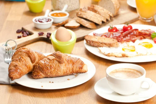 delicious breakfast with fresh tasty croissants, fried eggs with bacon, juice, coffee and sliced bread served on table