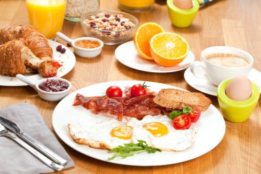 Kahvaltı servisi kruvasan, portakal suyu, çilek, haşlanmış yumurta ve domuz pastırması ve domates ile kızarmış yumurta ile müsli  