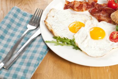 Sahanda yumurta ve pastırma beyaz tabak ve çatal bıçak damalı peçete ahşap masa üzerinde ile lezzetli kahvaltı