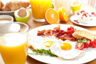 Sahanda yumurta ve domuz pastırması, ekmek, domates, müsli, portakal suyu ve masada haşlanmış yumurta ile lezzetli kahvaltı