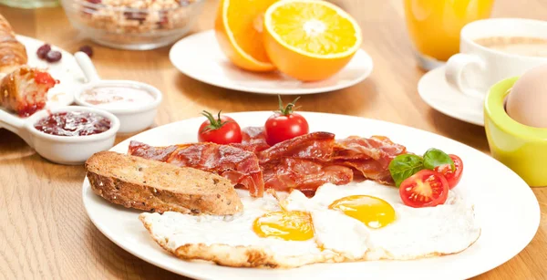 目玉焼きとベーコン チェリー トマト オレンジ ジュース コーヒー ゆで卵 ミューズリーのおいしい朝食のテーブルの上 — ストック写真