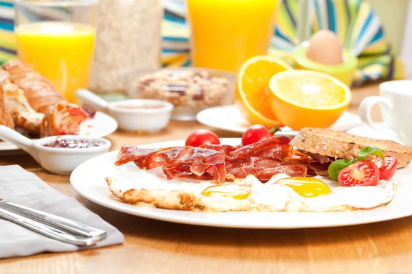 tasty breakfast with fried eggs and bacon, cherry tomatoes, orange juice, coffee, boiled egg and muesli served on table