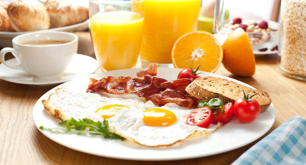 close-up view of fried eggs with bacon, bread and tomatoes, orange juice, coffee and croissants for breakfast 