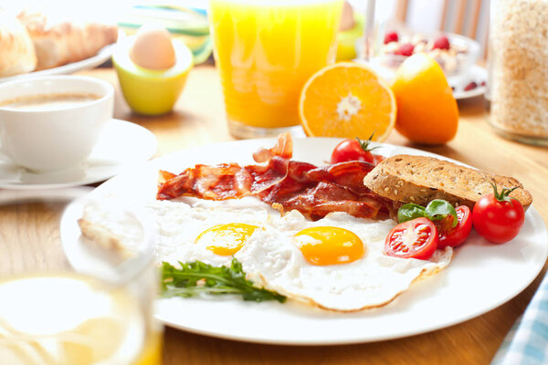 delicious breakfast with fried eggs and bacon, bread, cherry tomatoes, cup of coffee and orange juice on table