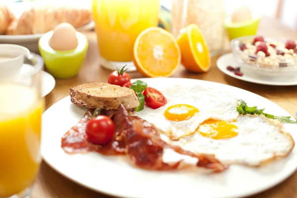 tasty breakfast with fried eggs and bacon, bread, cherry tomatoes, muesli, orange juice and boiled eggs on table