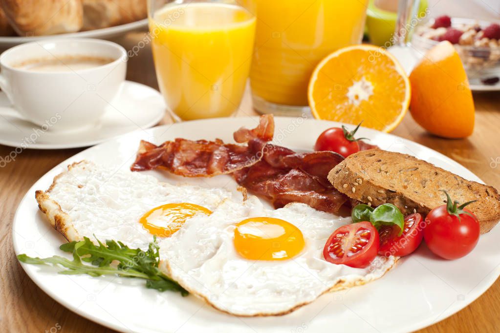 delicious breakfast with fried eggs and bacon, bread, cherry tomatoes, orange juice and coffee served on table